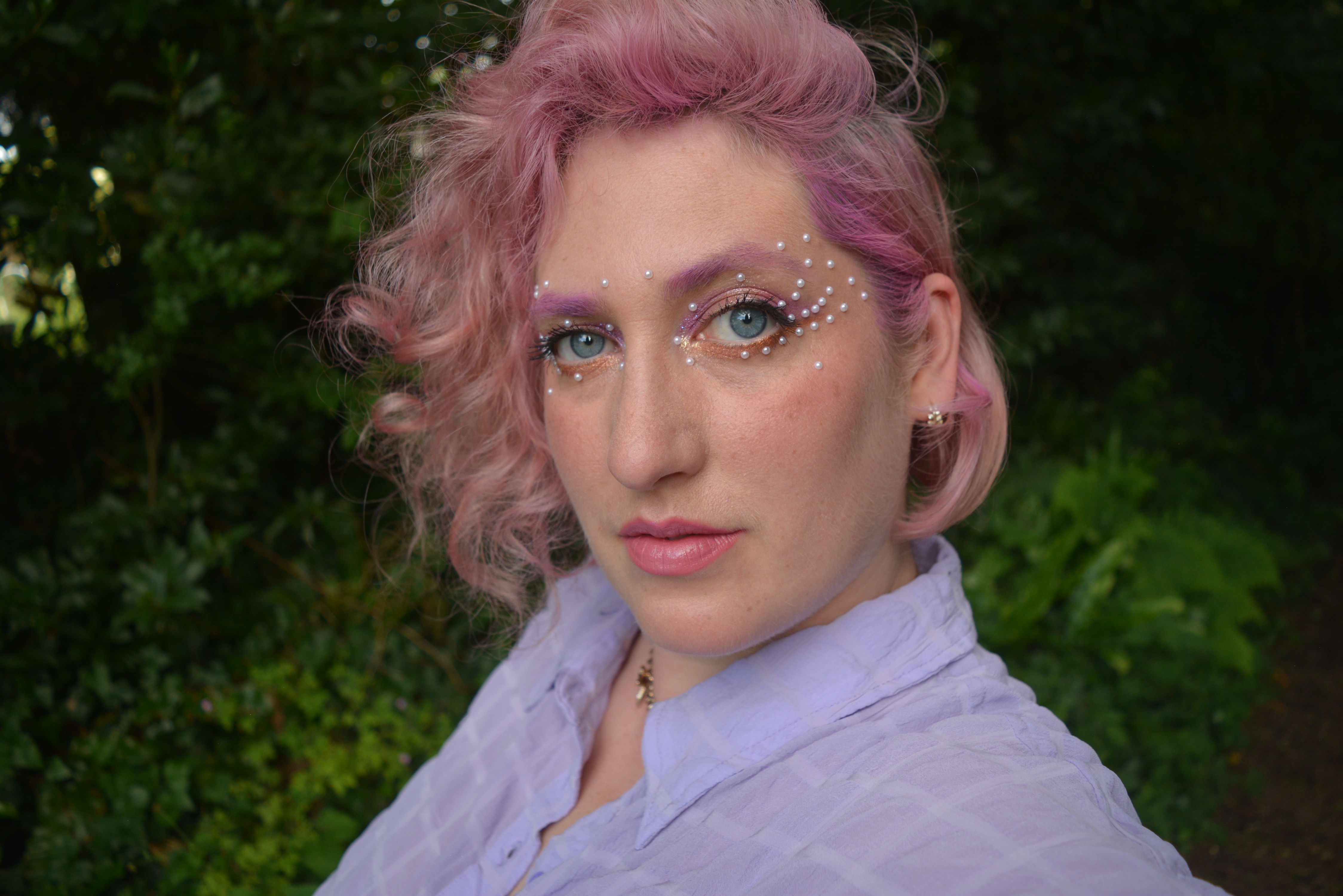 TeiFi against tree background, facing the camera, with decorative eye make up and pink hair