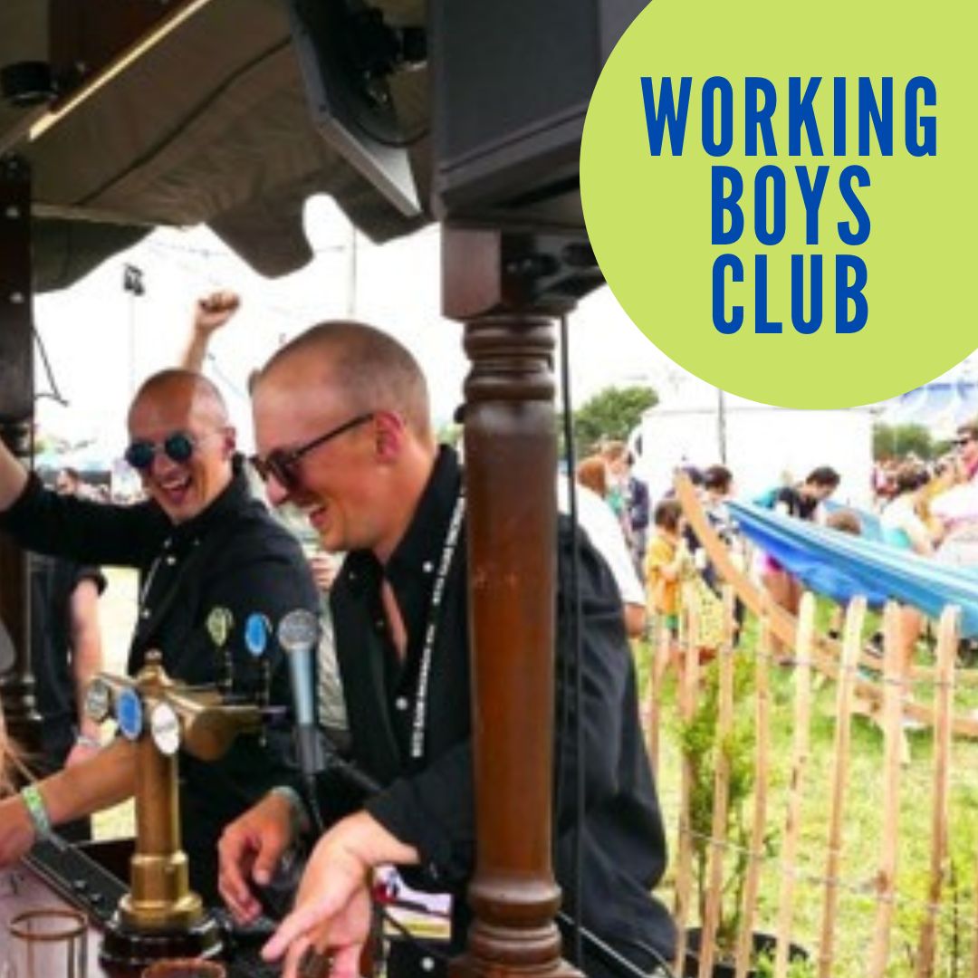 Photo of Working Boys Club. They're both standing at their interactive pub installation, wearing dark jackets and sunglasses.